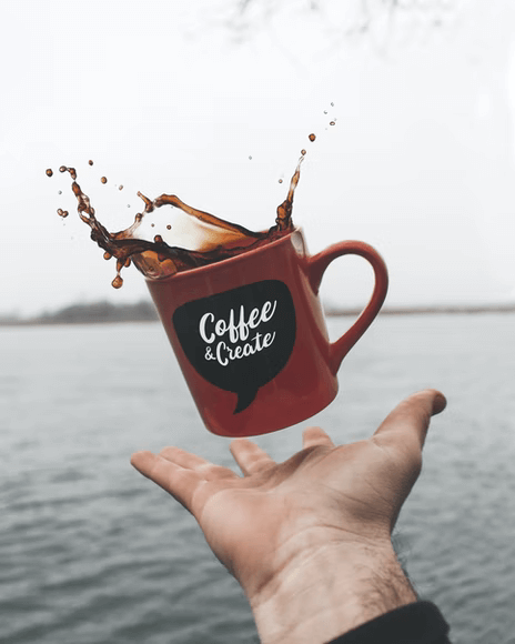 Branded coffee mug in air with coffee spilling, a hand reaching to catch it
