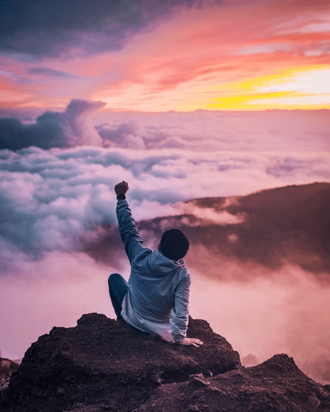 Person enjoying a vista of clouds and mountains while raising a hand in the air to celebrate.
