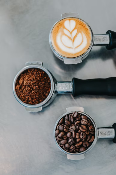 Photo of three coffee grinders, one with whole beans, ground coffee, and a latte.
