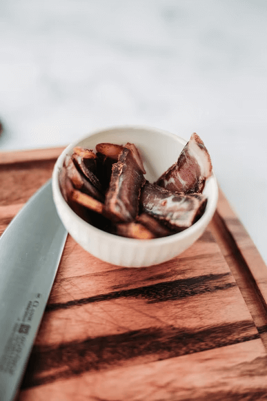 A bowl of prepared biltong on a cutting board alongside a chef's knife. 