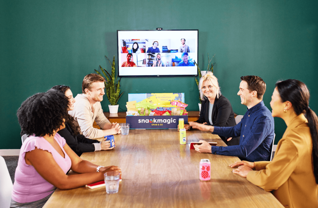 A hybrid workplace, with both virtual in-person coworkers talking with each other and sharing a large SnackMagic box.