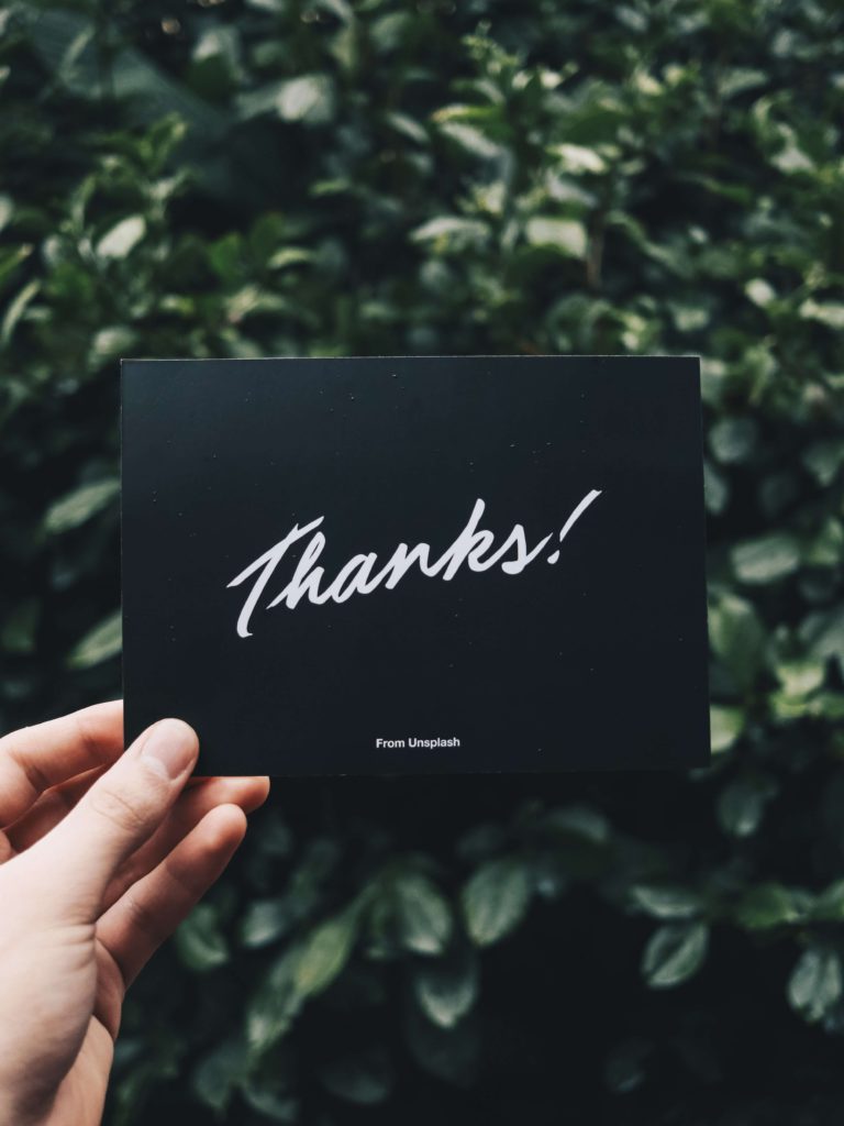 A gift card held up to a hedge, with a thank you sentiment on the cover. 