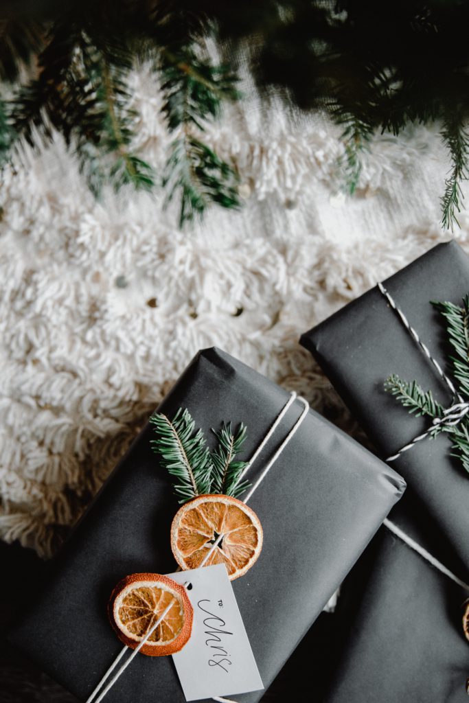 Elegant Christmas gifts arranged under a Christmas tree, decorated with seasonal pine and oranges.