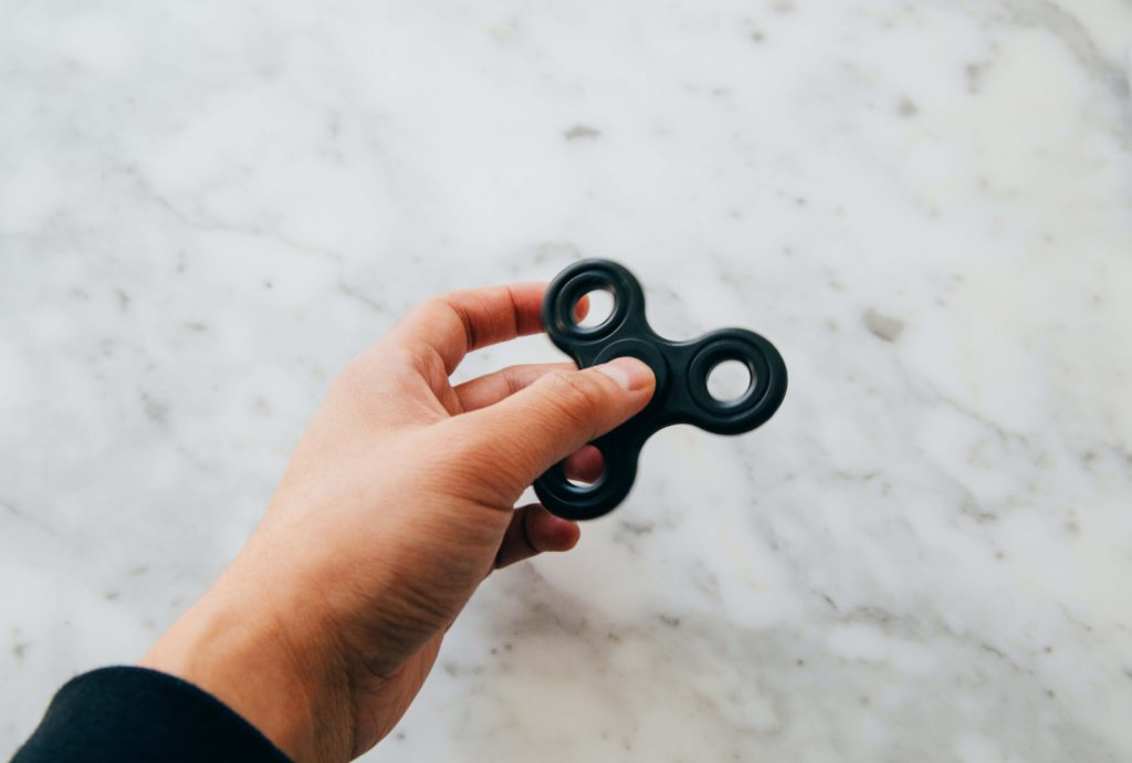 A hand holding a black fidget spinner against a white marble counter. 