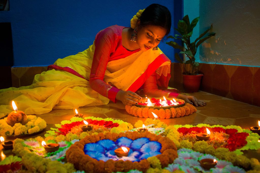 A woman with celebrating Diwali by lighting a candle among beautiful, traditional flowers.