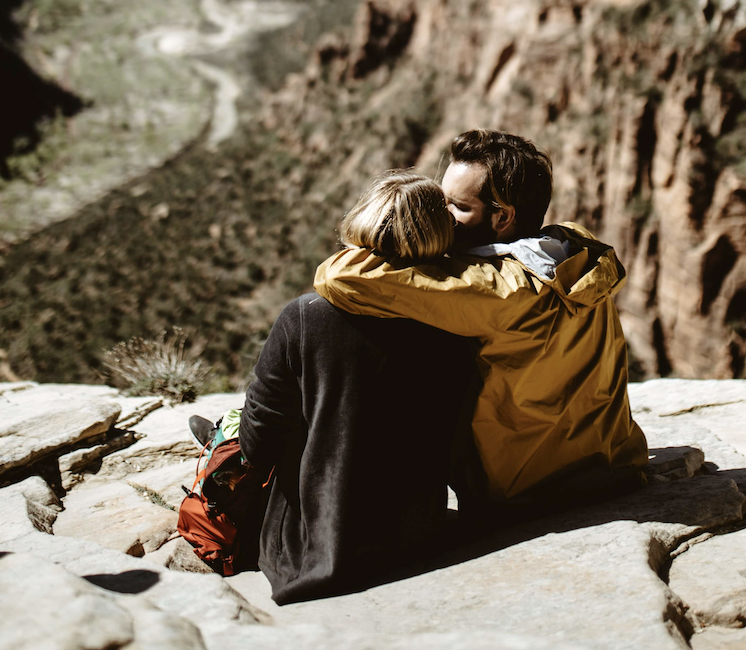 A couple on a hike enjoying each other's company and the view at the top of a mountain.