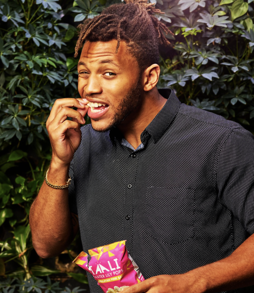 Young man taking a snack break outside infront of a hedge.
