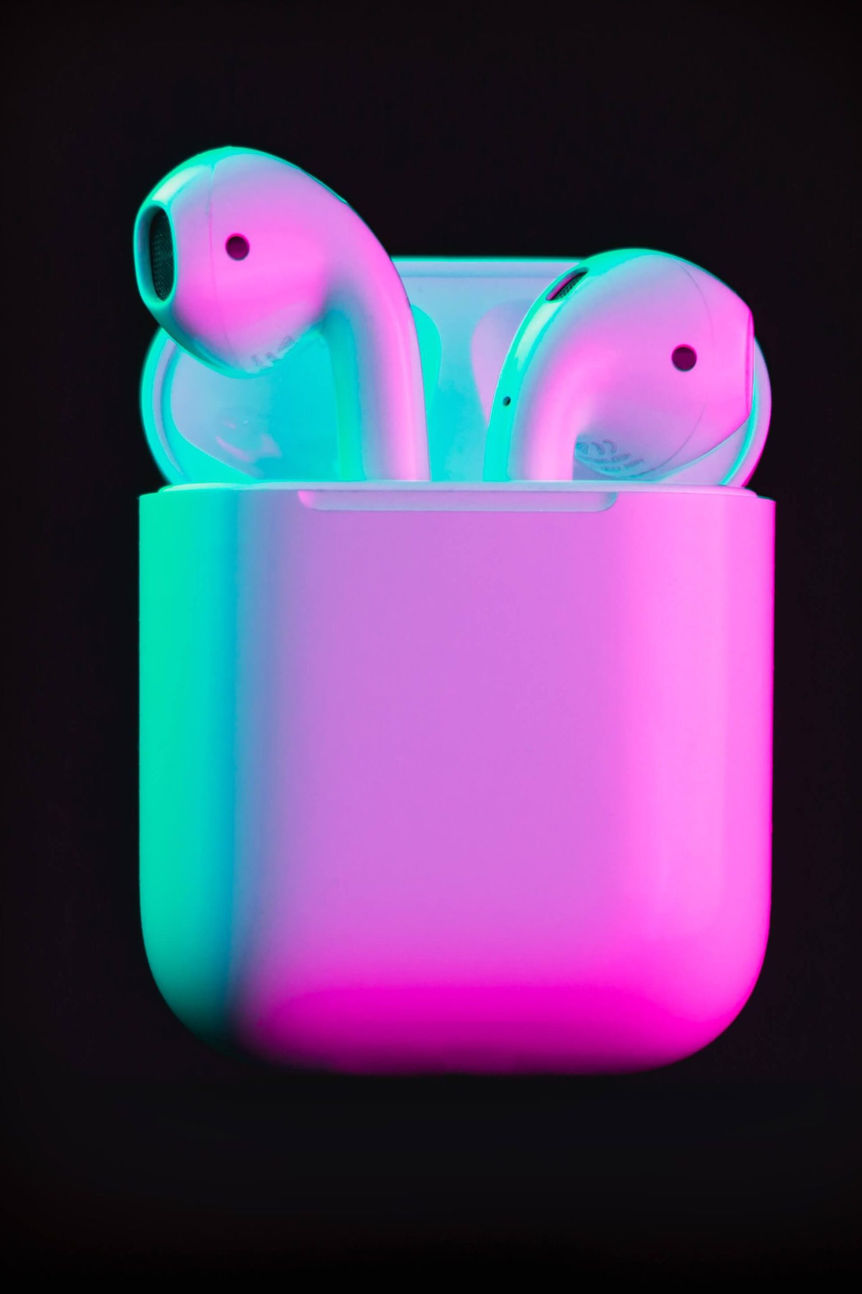 Apple Airpods against a black background illuminated by neon lighting for effect. 