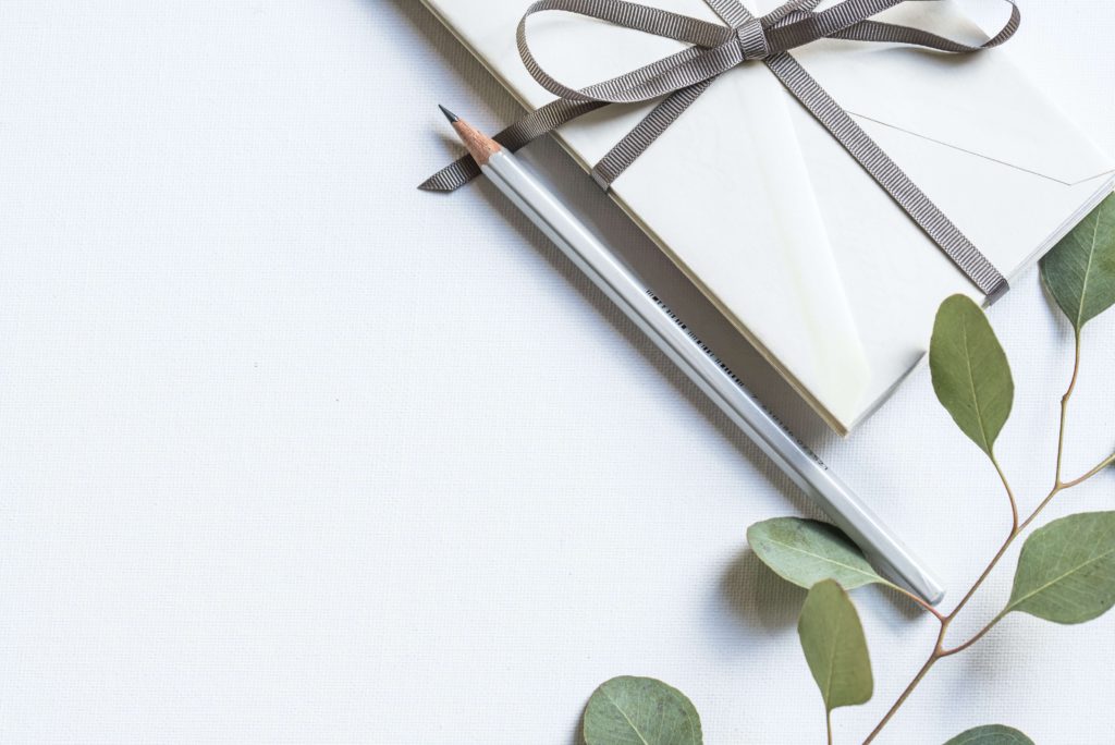 A business gift with a simple ribbon and newly sharpened pencil alongside a stem of eucalyptus. 