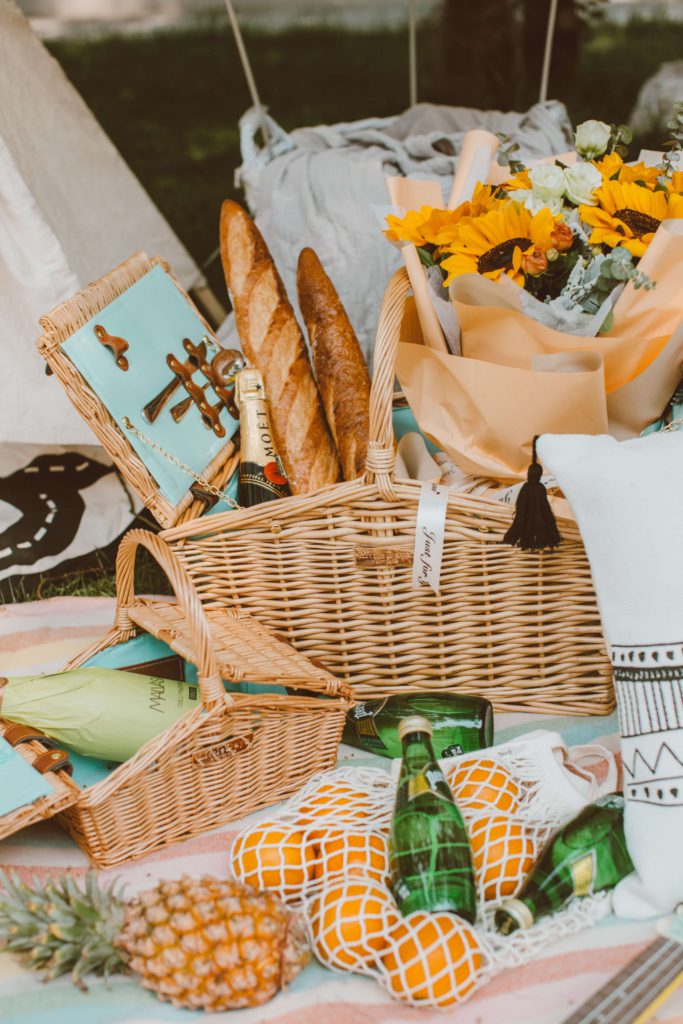 An outdoor, picnic-like spread of gift baskets full of fresh flowers, snacks, sparkling water, and more.