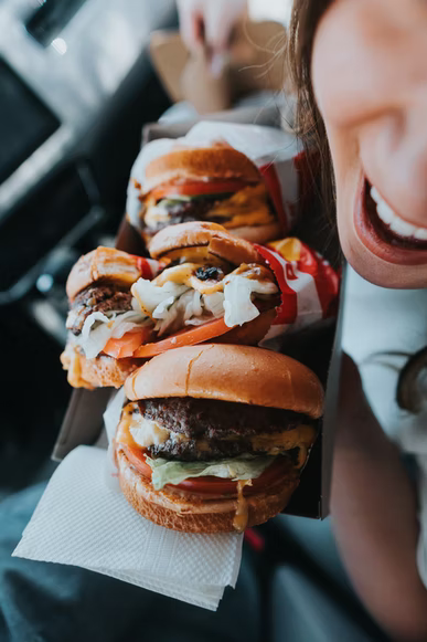 A young woman smiling and holding artisanal sliders full of meat, cheese, and toppings. 