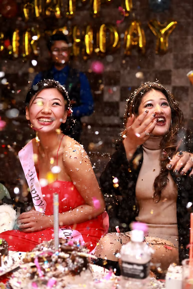 Two young women laughing and celebrating a birthday with confetti and treats at a restaurant.