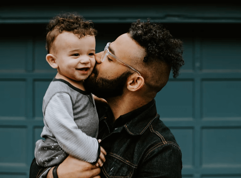 A young father holding his child and giving him a kiss on the cheek.