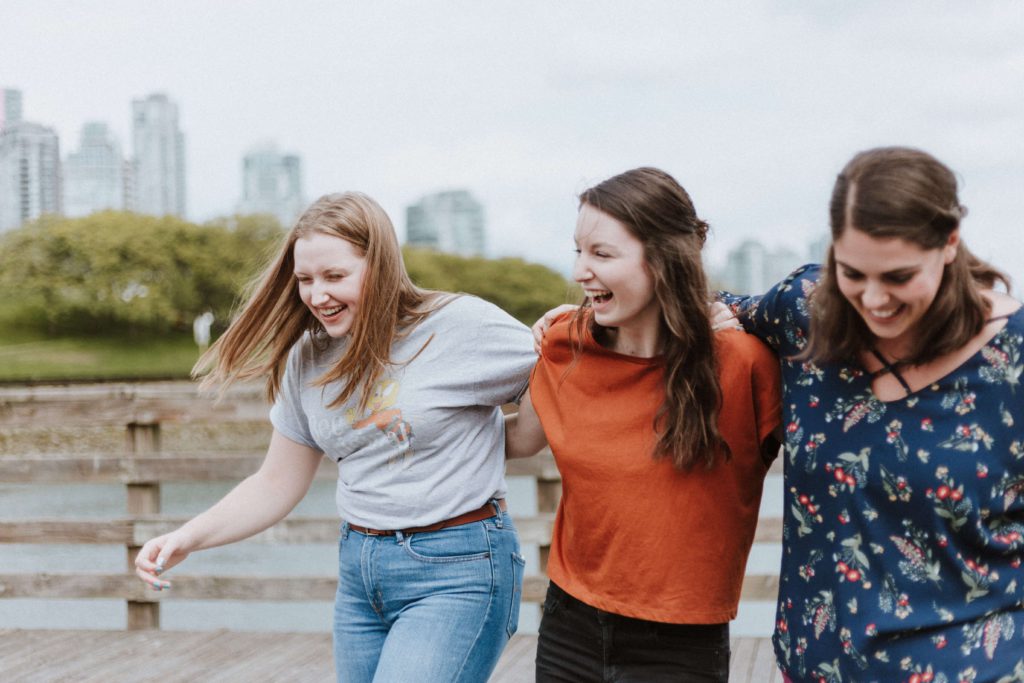 Three young women walking arm in arm, laughing and enjoying each other's company. 